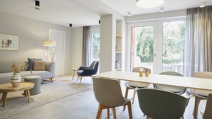 A modern living room with a sofa, a dining table with chairs, a coffee table, and a lamp. - Bades Huk (Hohenkirchen)
