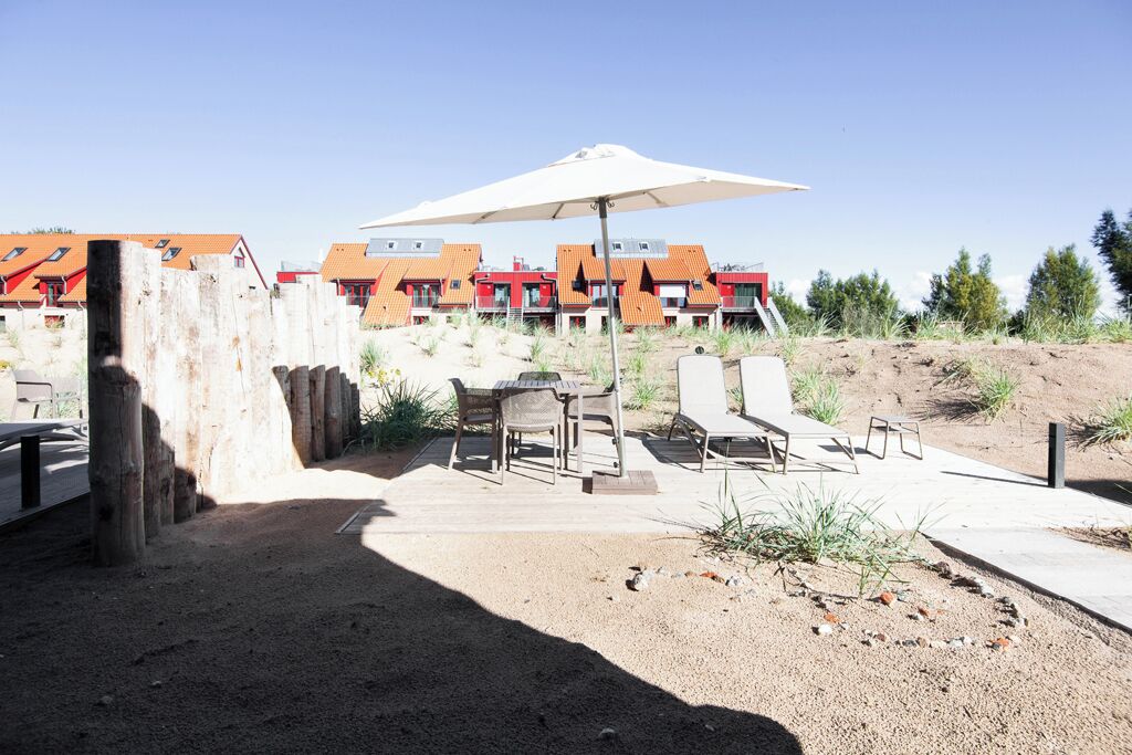 A patio area with outdoor furniture, a large umbrella, and a row of buildings with red roofs in the background.