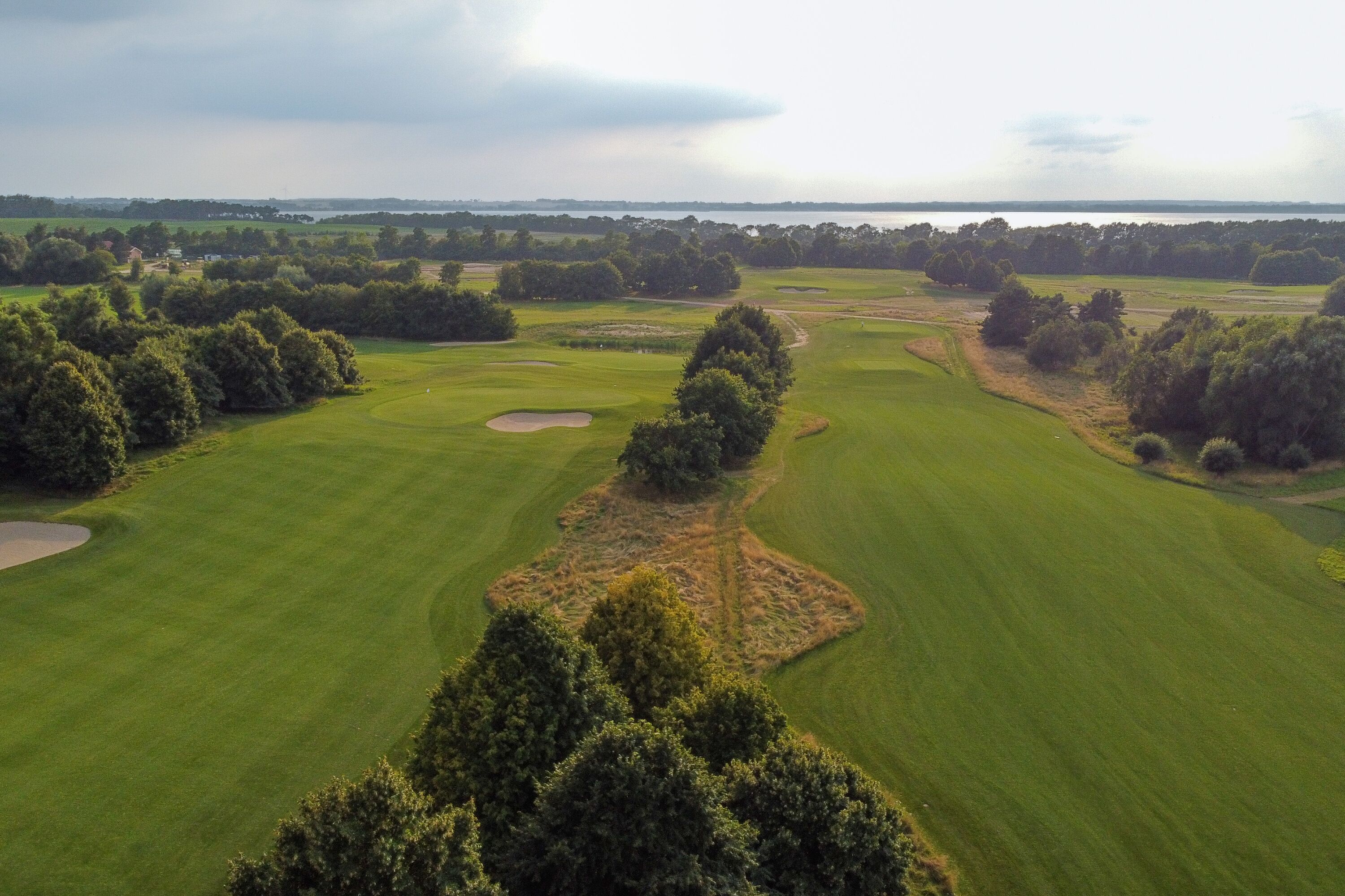 A golf course with multiple holes, trees, and a body of water in the background.