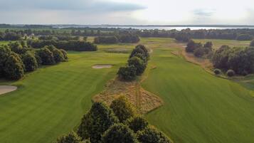 Een golfbaan met meerdere holes, bomen en een waterpartij in de achtergrond.