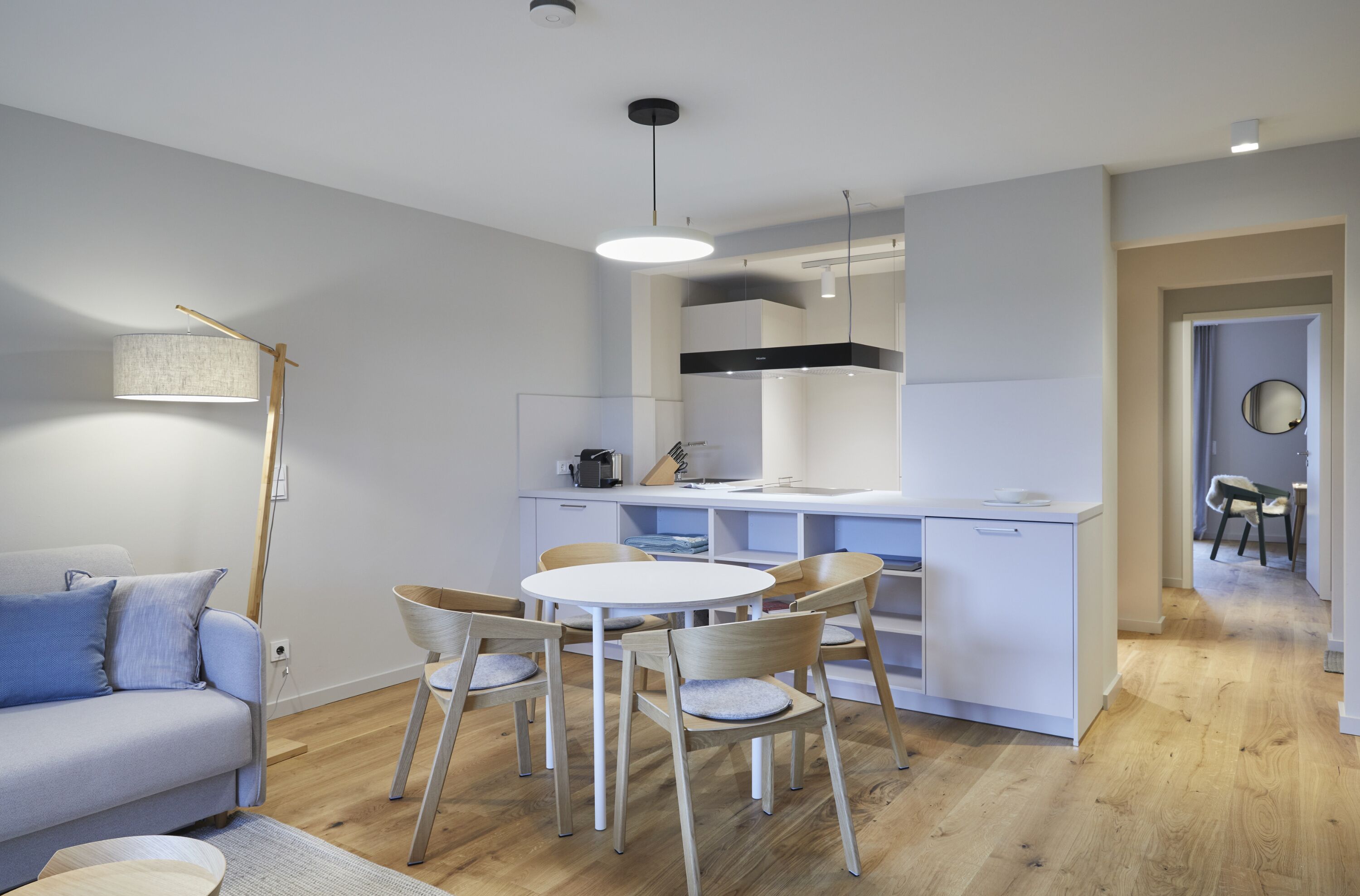 A modern kitchen with white cabinets, a dining table with chairs, and a built-in oven.