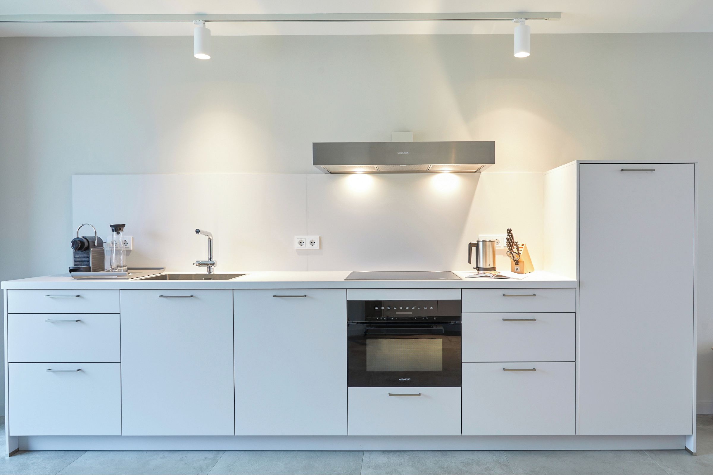 Een moderne keuken met een ingebouwde oven, een koffieapparaat en een waterkoker op het aanrecht.