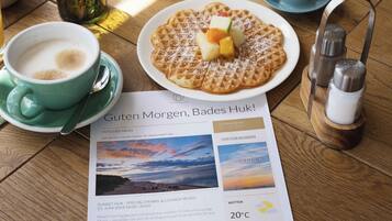 Een ontbijtje met een wafel, fruit en koffie op een houten tafel.