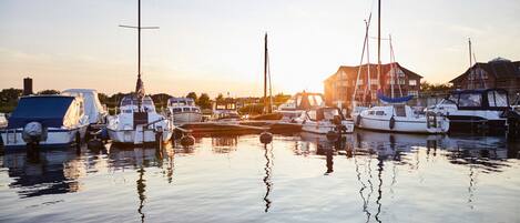 A marina with several boats docked, calm water, and a building in the background.