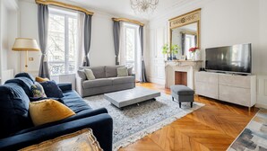 A living room with a sofa, a coffee table, a TV, and a fireplace. - Porcelain Pelouse, by Veeve (Paris)