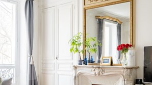 A living room with a fireplace, a large mirror, and a grey ottoman. - Porcelain Pelouse, by Veeve (Paris)