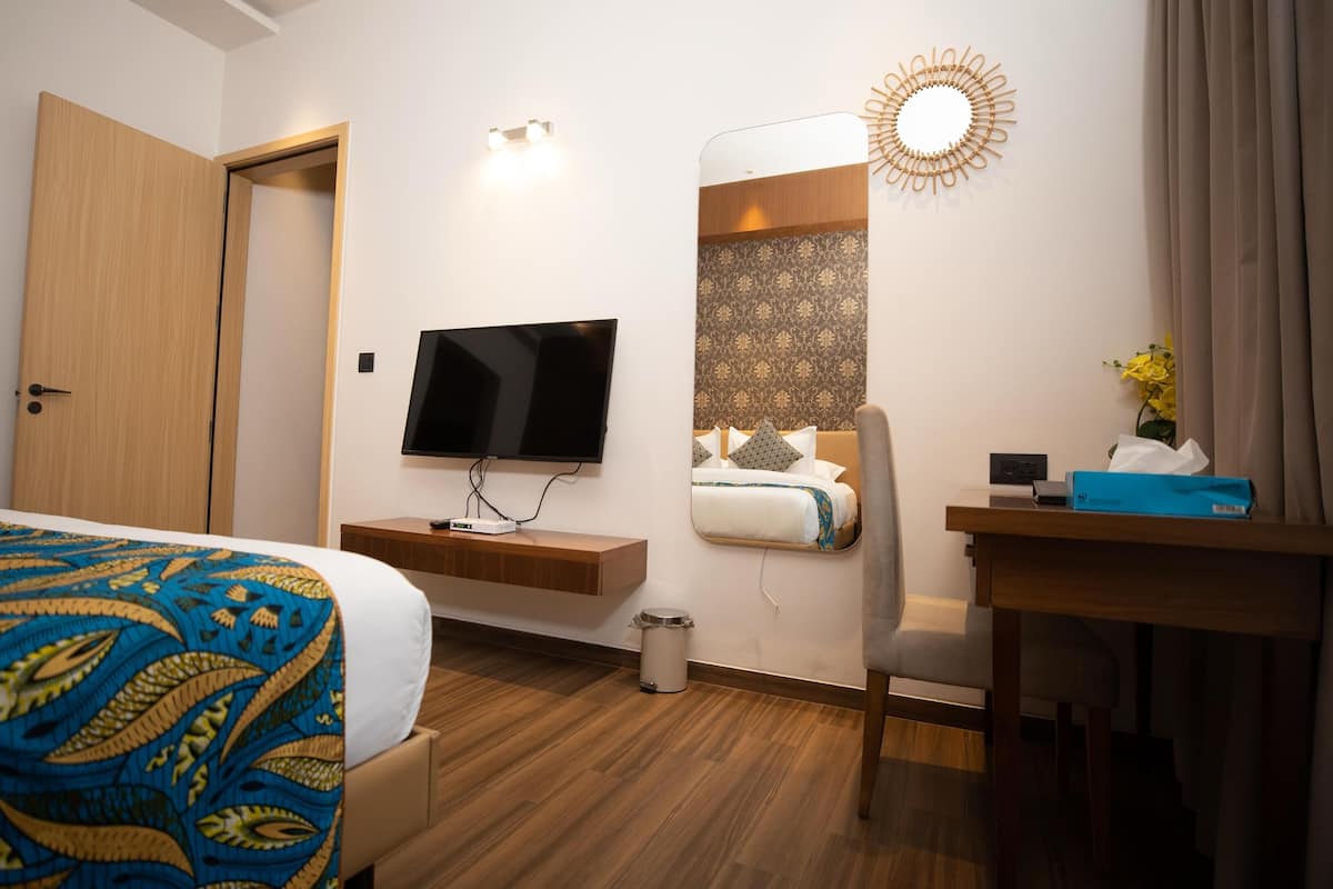 Habitació d'hotel amb un llit, una taula de nit, un televisor, un mirall i una làmpada penjada a la paret.
