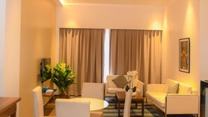 A modern living room with a sofa, armchairs, a coffee table, and a TV. There are curtains on the windows and a painting on the wall. - Aqua Inn (Kinshasa)