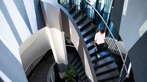 A modern interior with a spiral staircase, a potted plant, and a person descending. - ARTOTEL Grand Prima Surabaya (Surabaya)