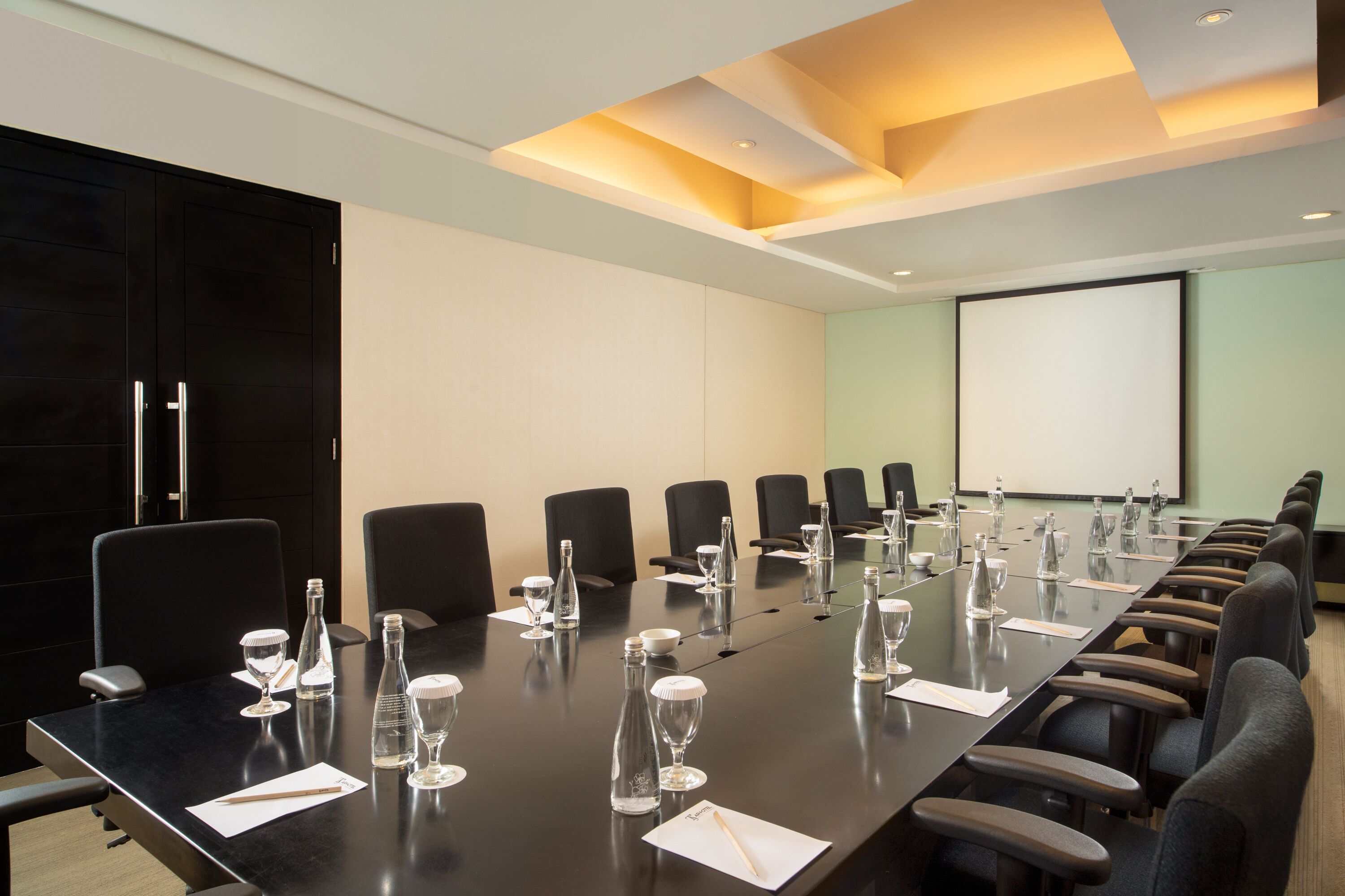 A conference room with a long table, chairs, and a projector screen.
