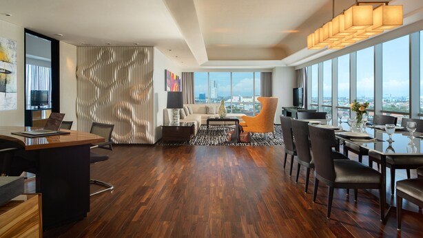 A modern hotel room with a large city view, a dining area, and a cozy seating area with a sofa and armchairs. - ARTOTEL Grand Prima Surabaya (Surabaya)