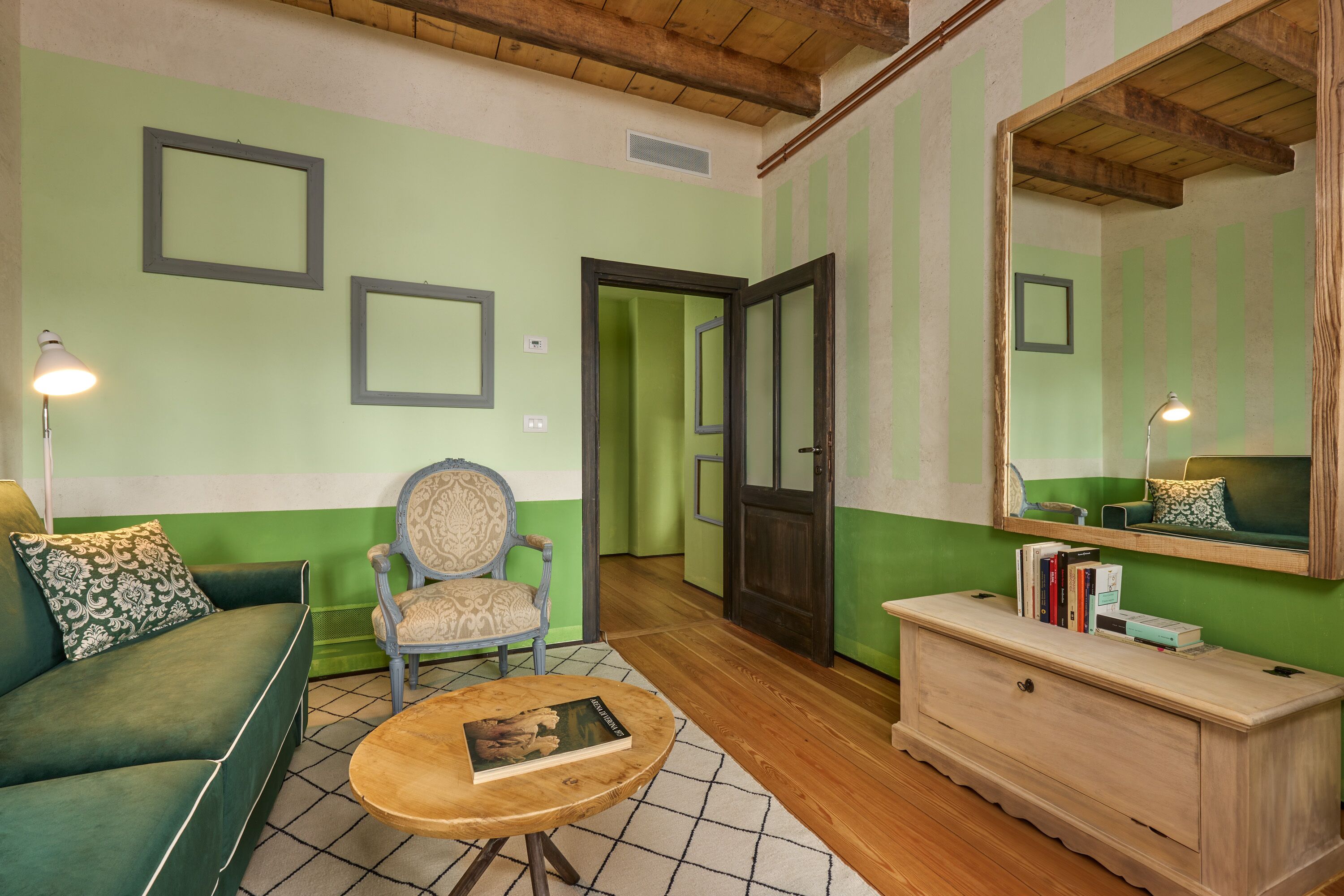 A living room with a green sofa, a wooden coffee table with a book, a chair, a wooden cabinet, and a mirror on the wall.