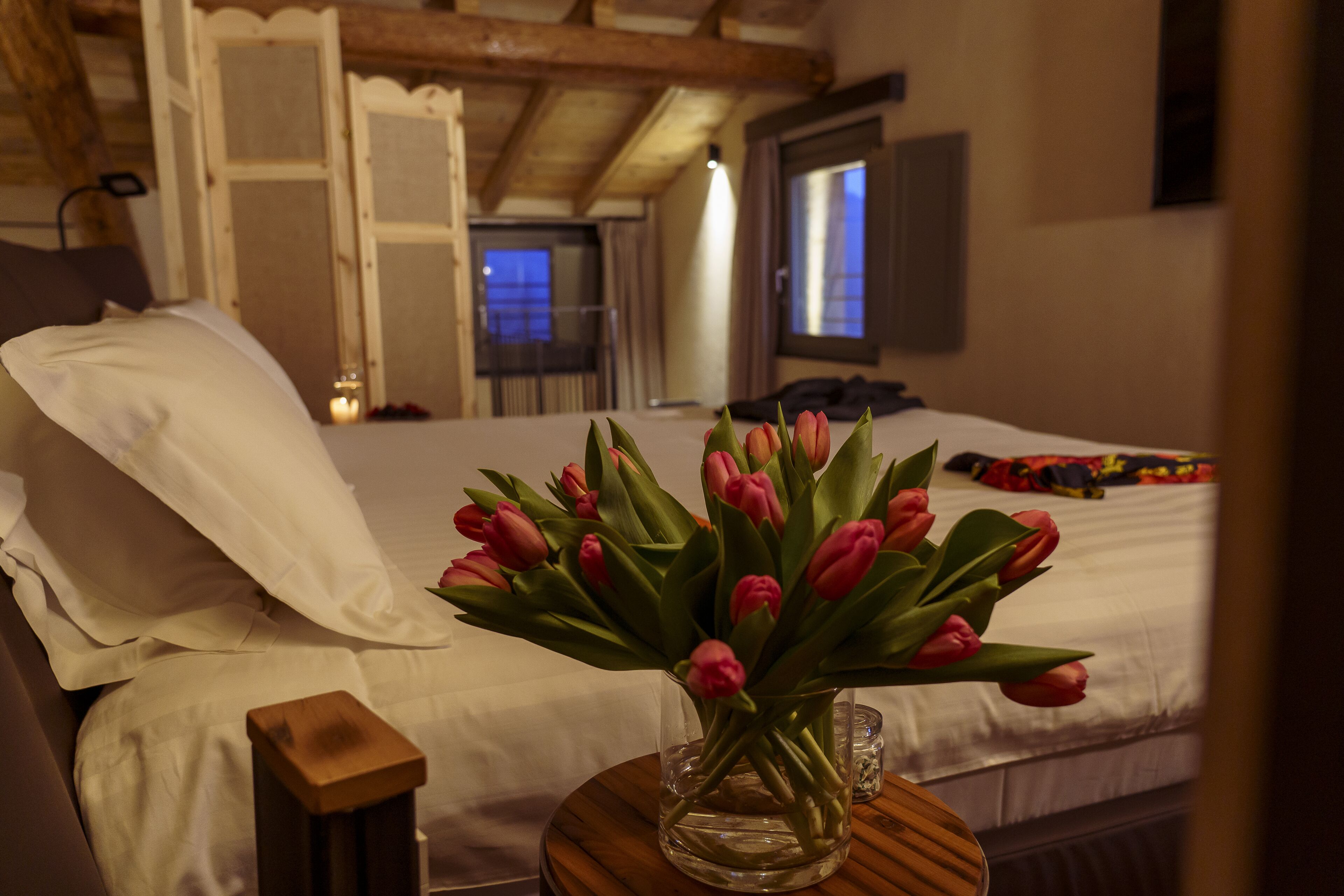 Une chambre à coucher avec un lit, une table de chevet en bois et un vase de tulipes.