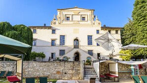 A large building with a stone wall, outdoor seating, and a staircase leading to the entrance. - Villa Balis Crema (Grezzana)