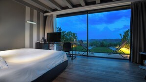 A bedroom with a large bed, a desk with a TV, and a sliding glass door leading to an outdoor area with a lawn and chairs. - Villa Balis Crema (Grezzana)