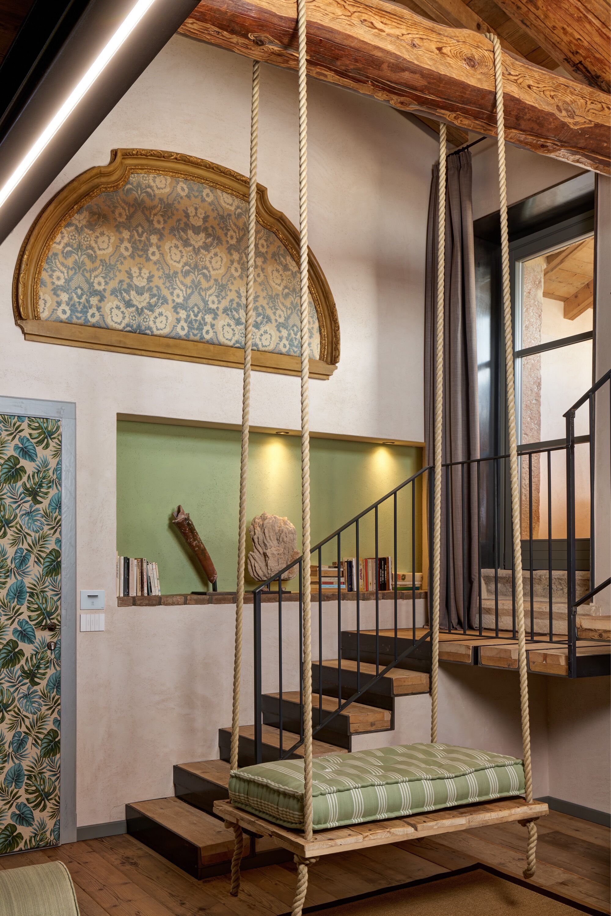 A wooden staircase with a swing seat, a patterned wall, and a green shelf with books.