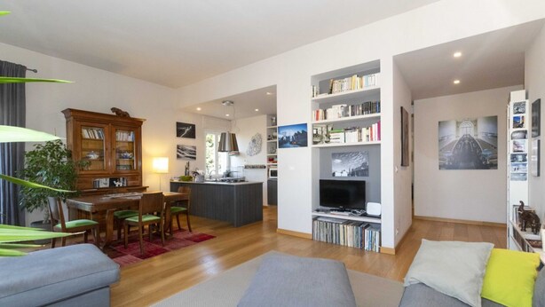 A modern living room with a sofa, ottoman, dining area, kitchen, and entertainment unit.