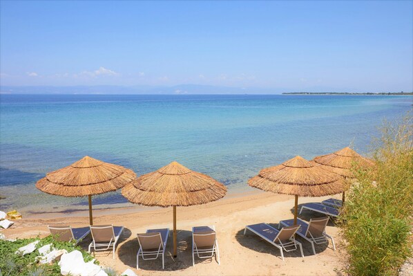 A beach with thatched umbrellas and sun loungers facing the sea.