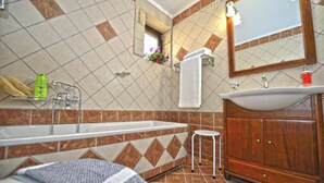 Un baño con bañera, lavamanos, espejo y una pequeña ventana con flores.