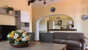 Una sala de estar con un sofá, una mesa de comedor con un centro de mesa floral, y una cocina visible a través de un arco.