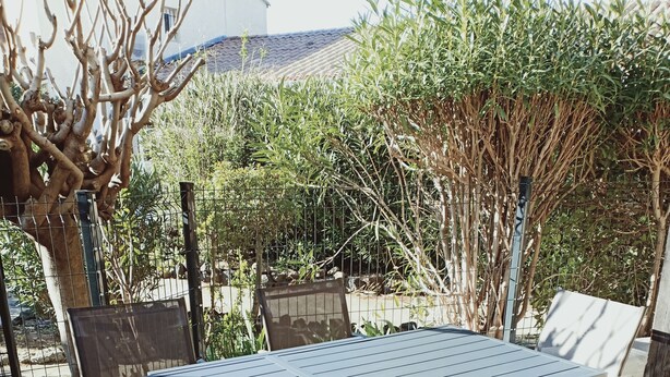 An outdoor patio with a table and chairs, surrounded by stone flooring and various plants. - Superb T2 on garden level in private residence with swimming pool (Cap d'Agde)