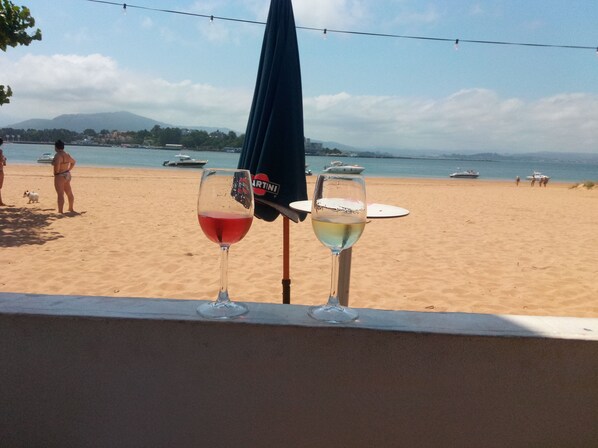 Deux verres à vin sur un balcon donnant sur une plage où l’on aperçoit des bateaux sur l’eau.