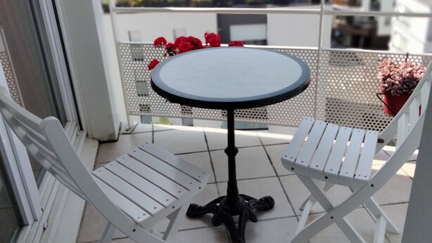Een balkon met een ronde tafel en twee witte stoelen.