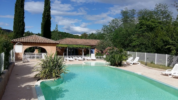 En swimmingpool med liggestole, et pergola og en bygning med et tag af fliser.