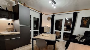 Et moderne køkken med spiseplads, med et træbord og stole, indbygget ovn og et stort vindue med gardiner.