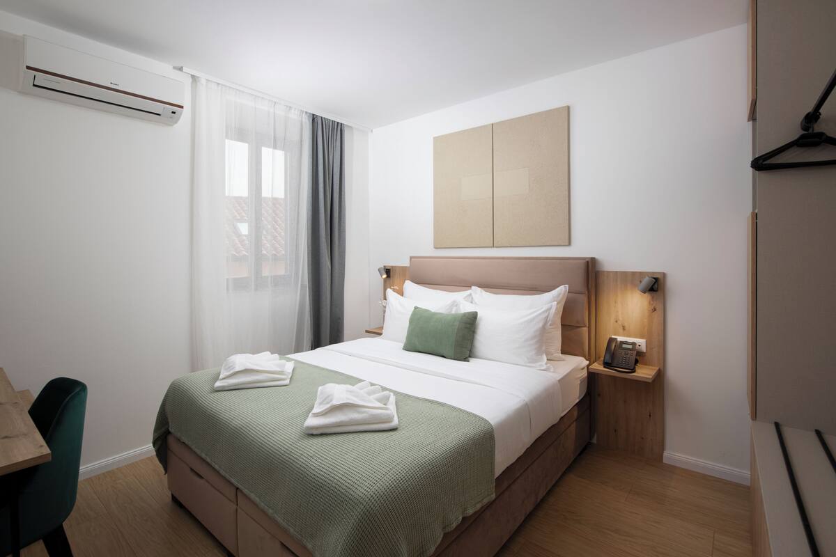 A hotel room with a bed, bedside table, and a wall-mounted phone.