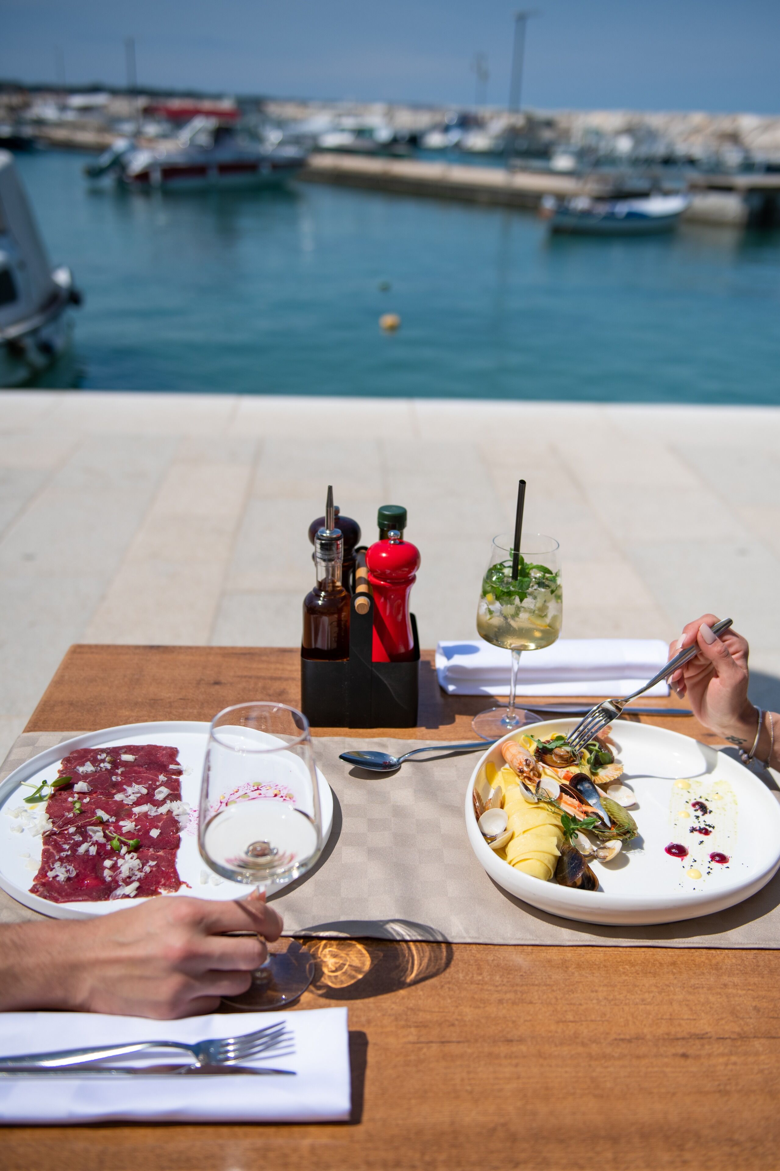 A dining table with plates of food, a wine glass, and condiments.