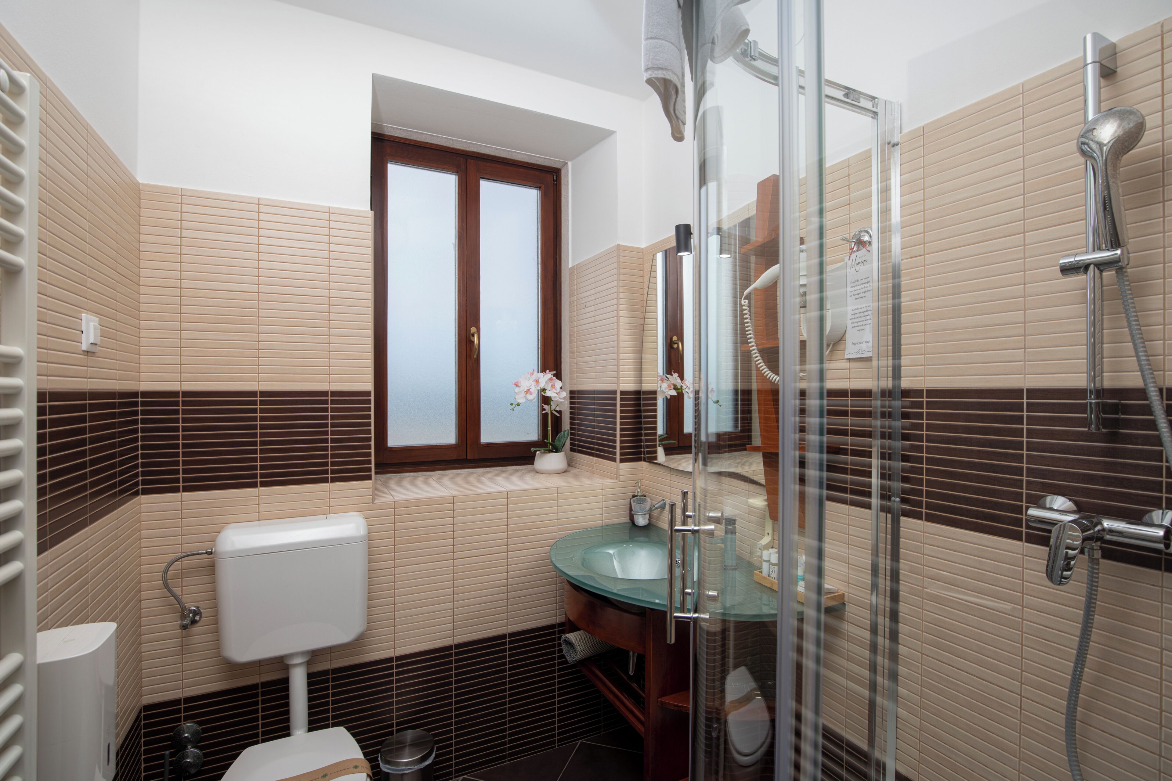 Une salle de bain équipée de toilettes, d’un lavabo, d’une douche et d’une fenêtre donnant sur un paysage agréable.