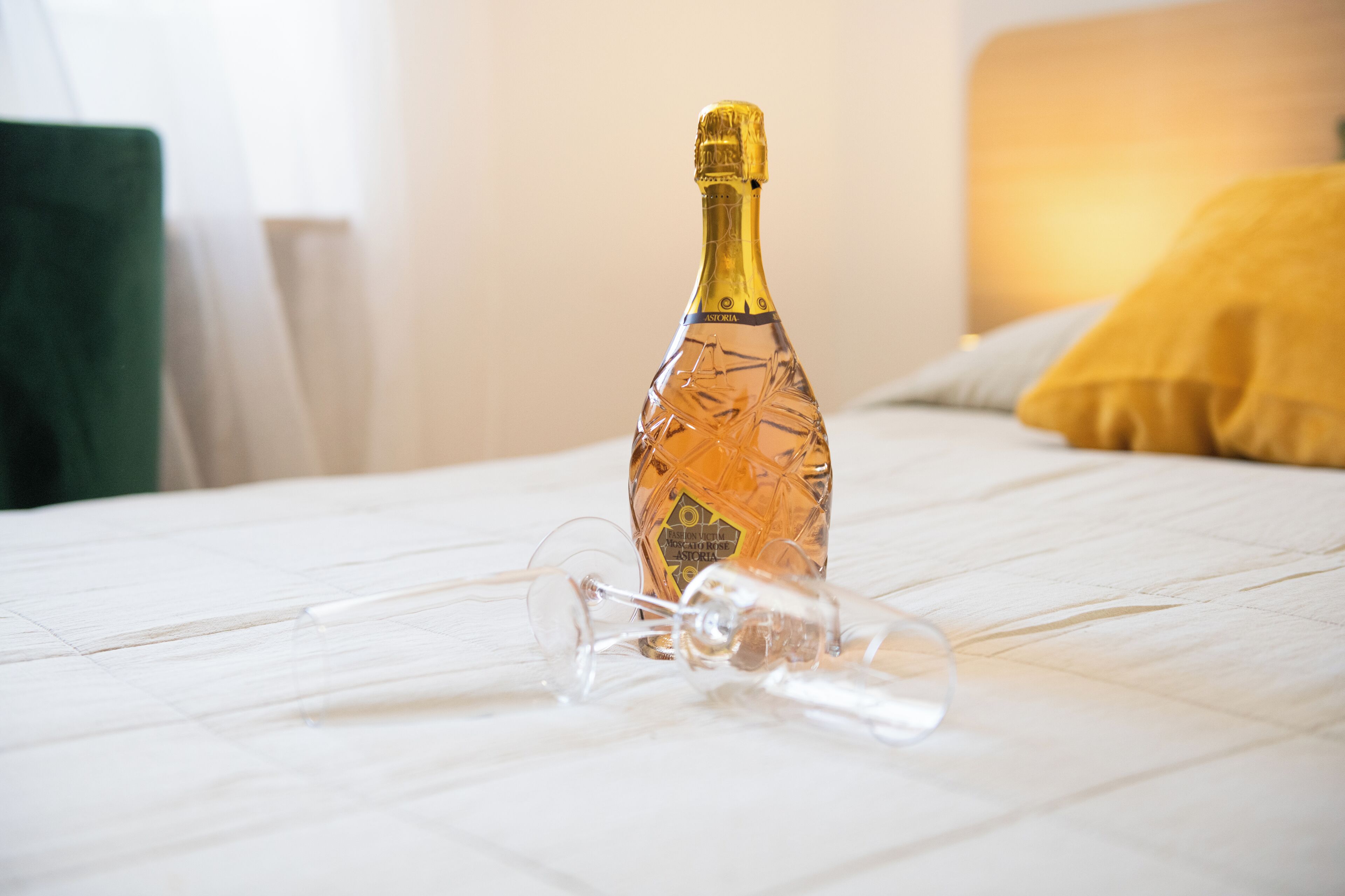 A bottle of champagne on a bed with a clear glass and a straw.