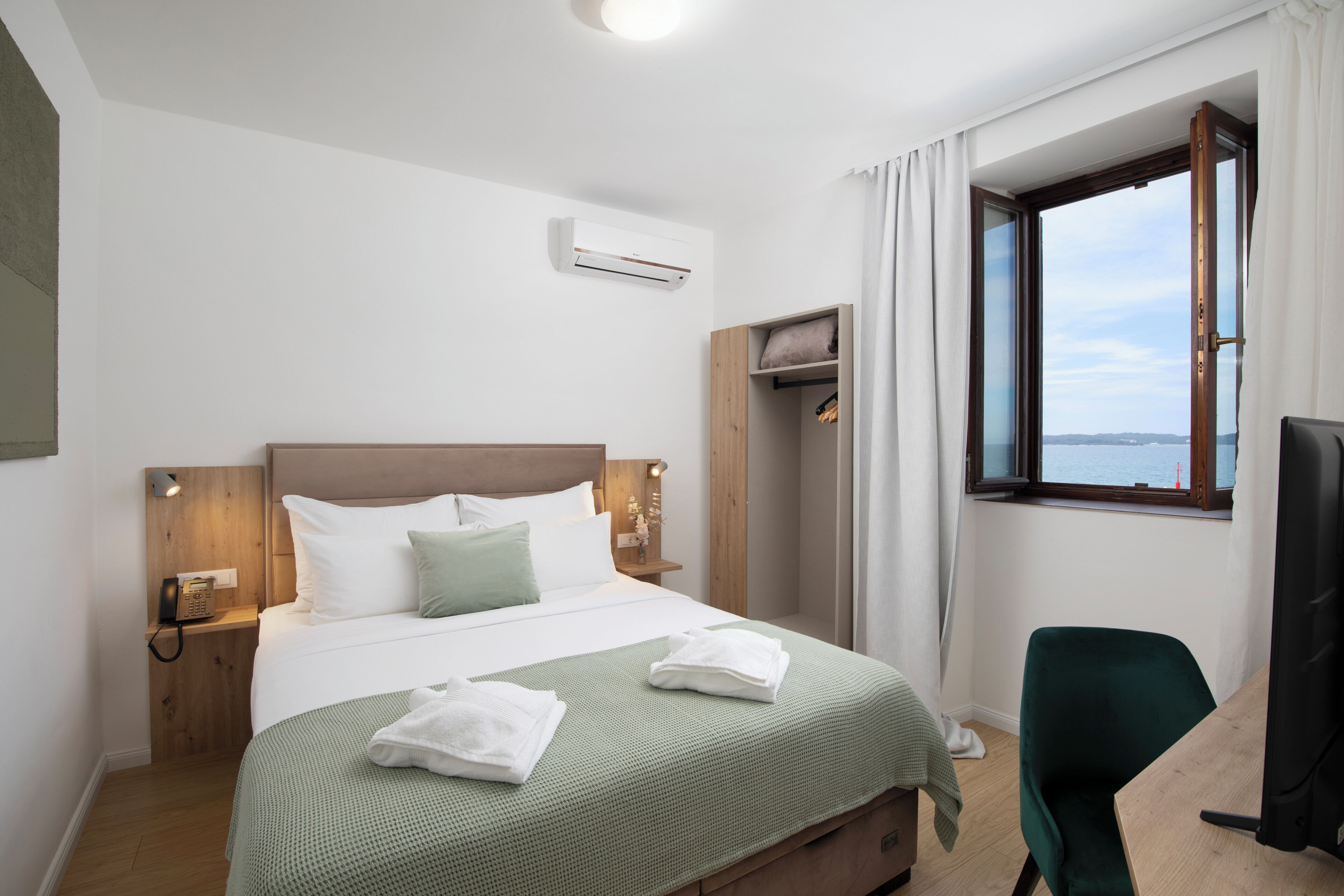 Una camera d'albergo con un letto, una scrivania, una sedia, una finestra con tende e vista sul mare.