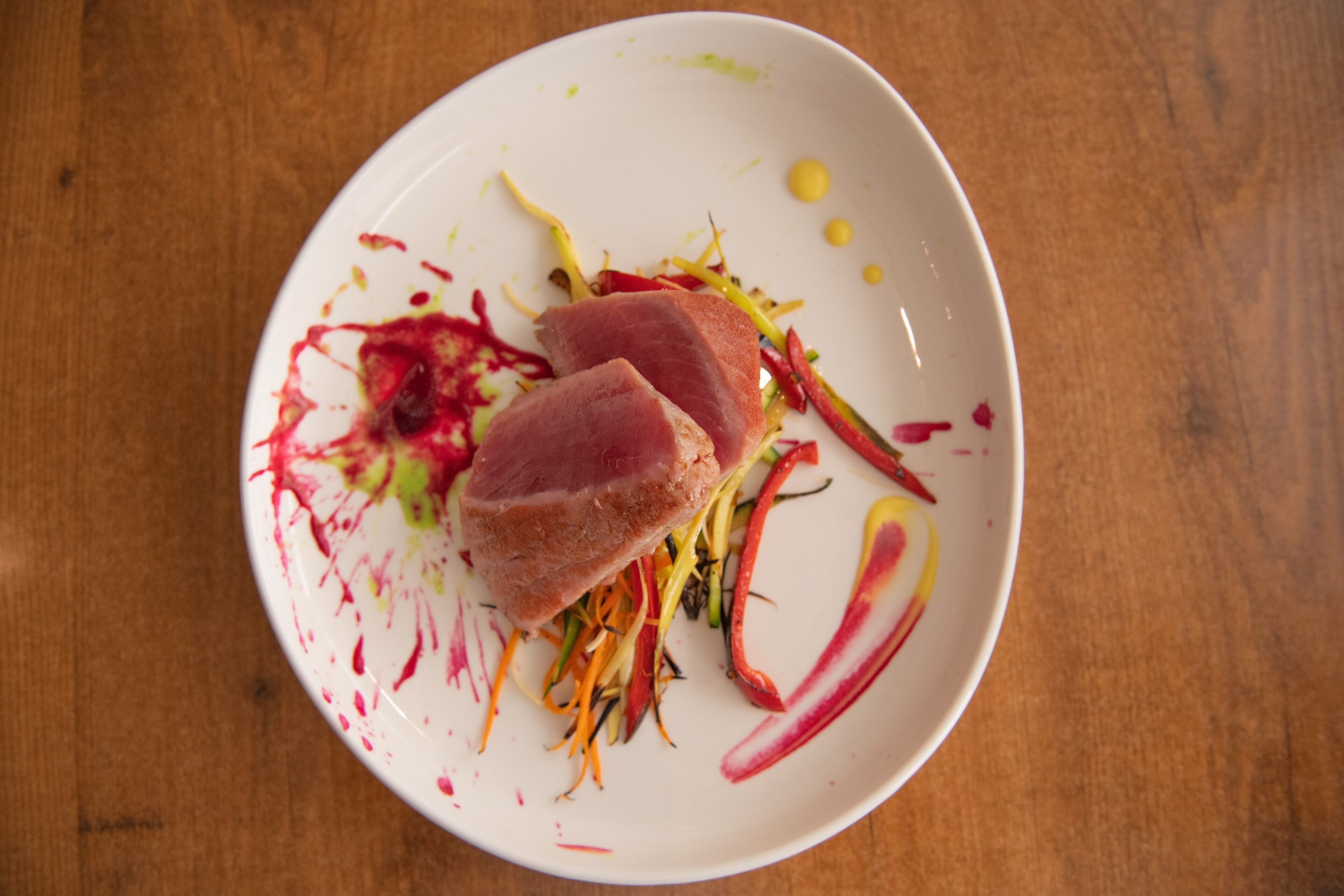 A white plate with a piece of meat, vegetables, and a sauce on a wooden table.