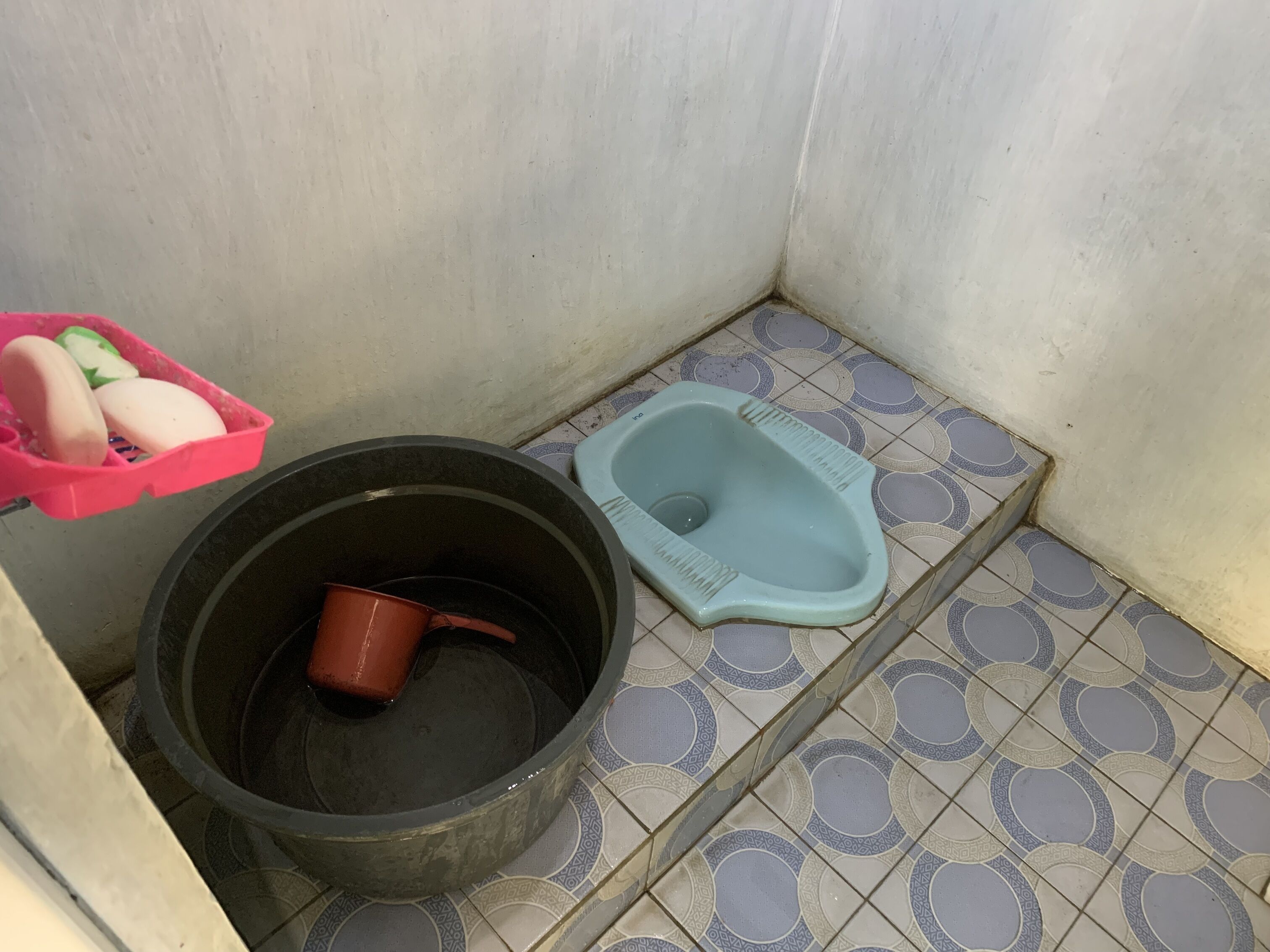A small bathroom with a toilet, a bucket, and a basin.