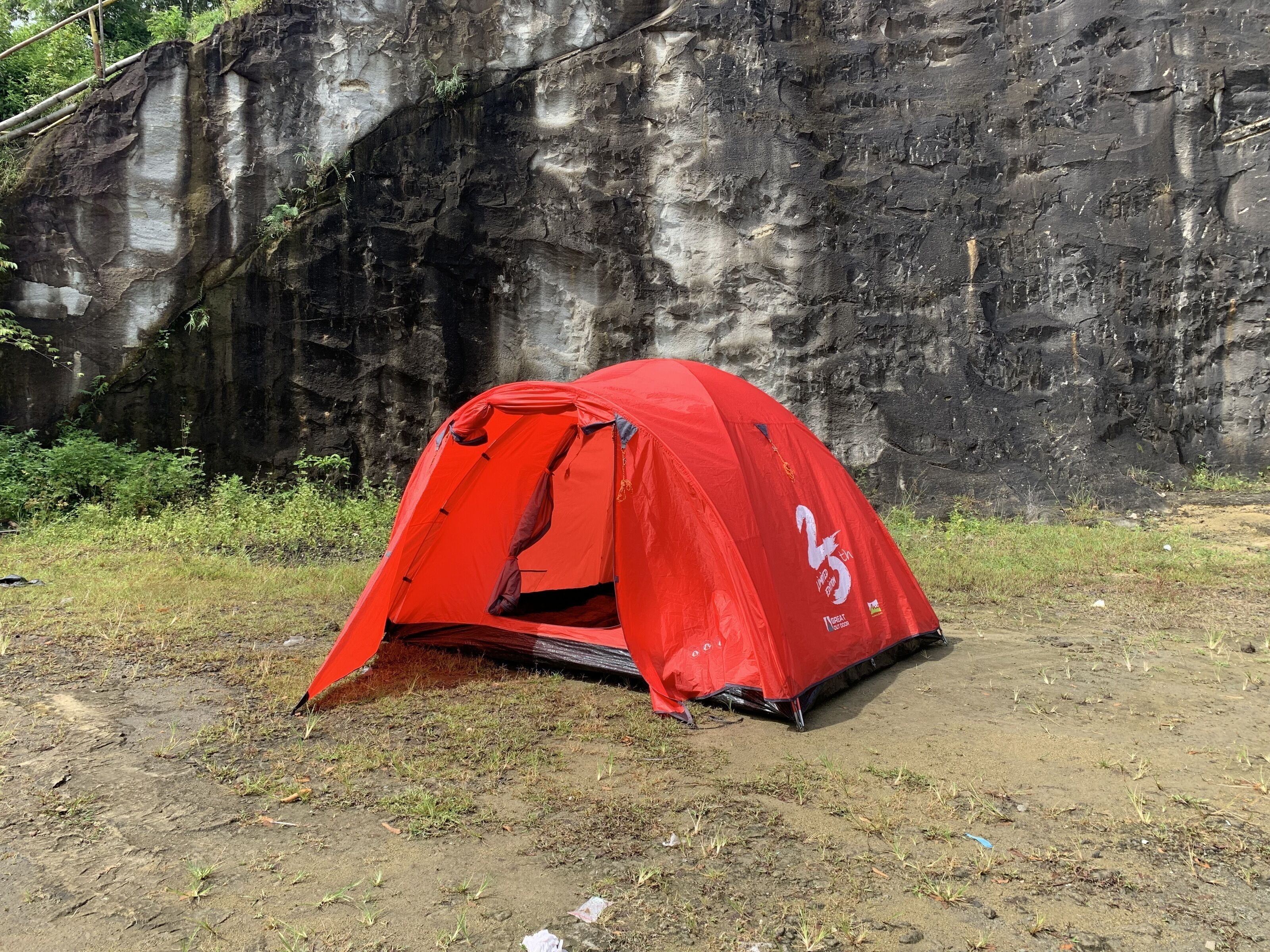 A red tent set up on a dirt ground with a rocky cliff in the background.