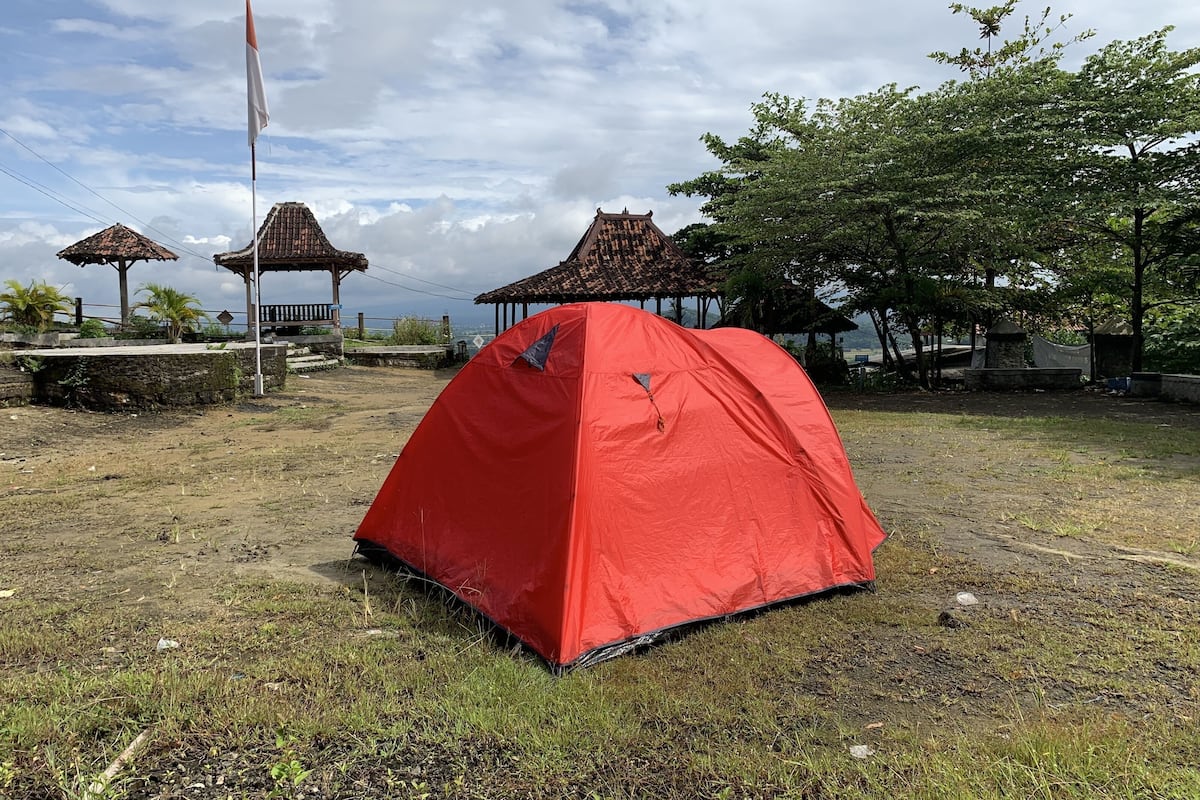 A red tent in a grassy area with traditional-style structures in the background.