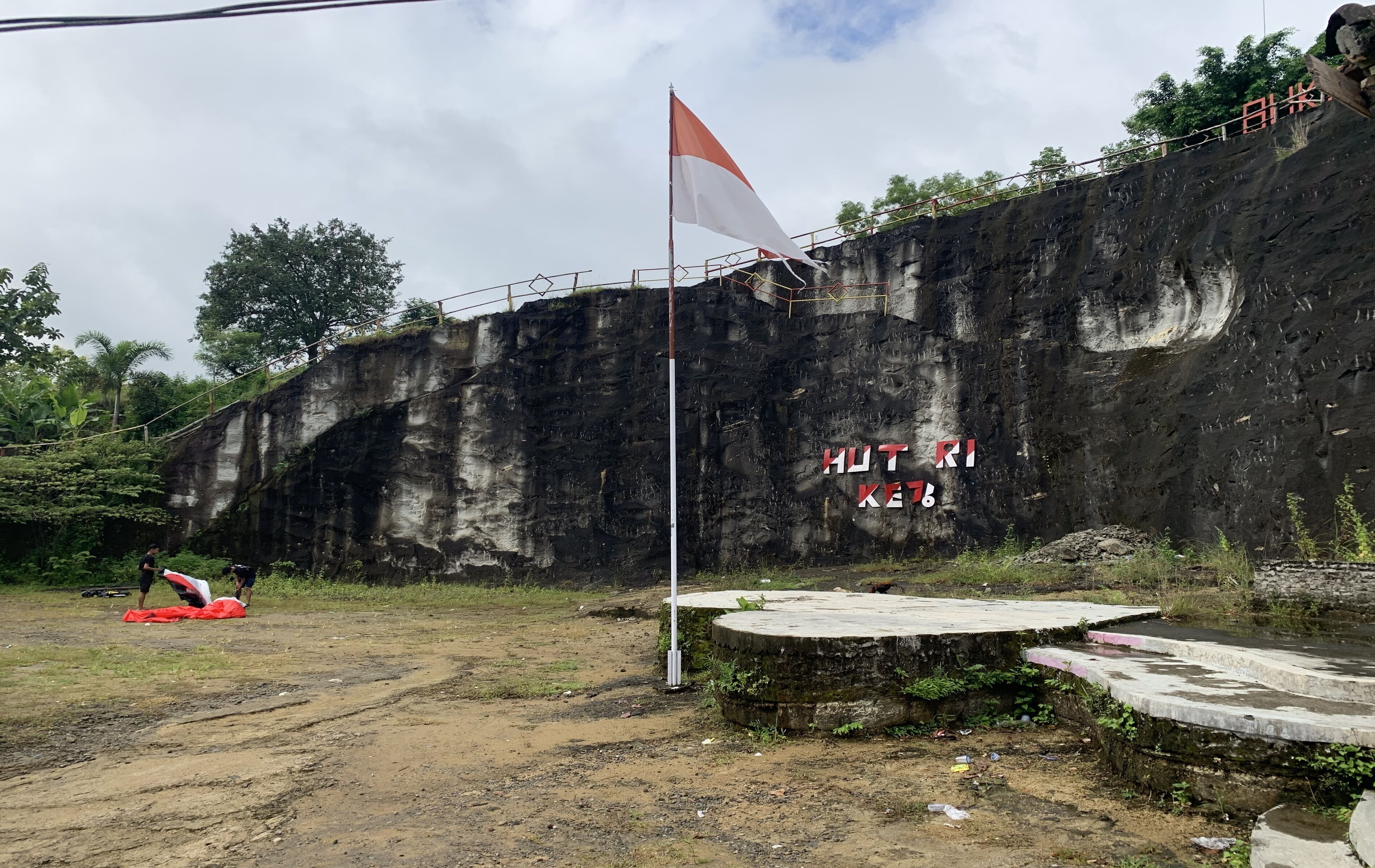 A flagpole with a flag, a rocky cliff, and a paved area with steps.