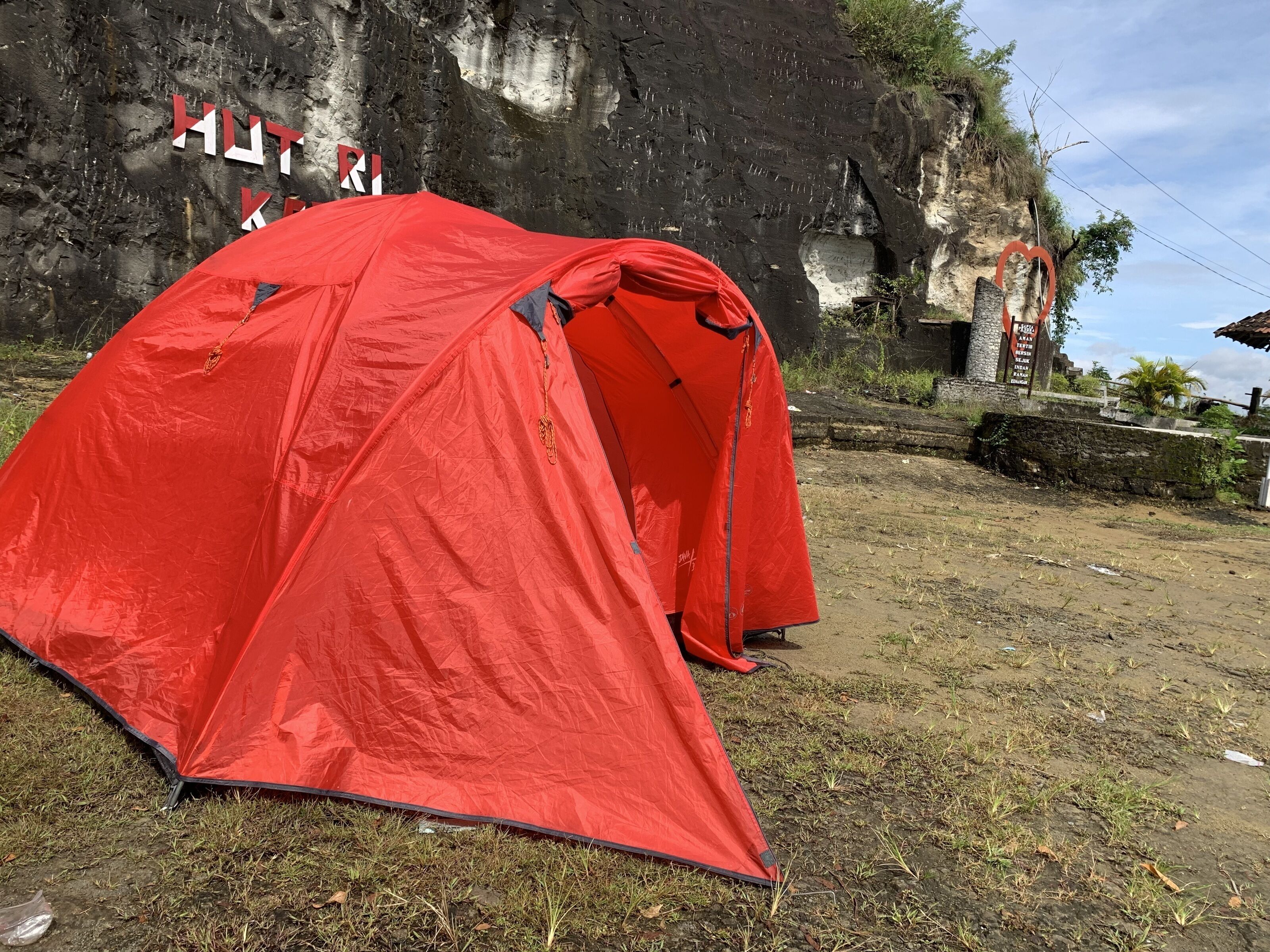 Una tenda rossa montata su una zona erbosa, con una scogliera rocciosa sullo sfondo.
