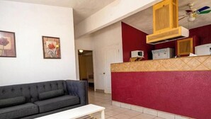 Ein Wohnzimmer mit einer Couch, einem kleinen Tisch und einer Küchenzeile mit Schränken und Geräten.