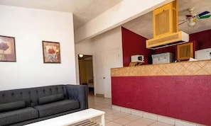 A living room with a sofa, a small table, and a kitchen area with cabinets and appliances.