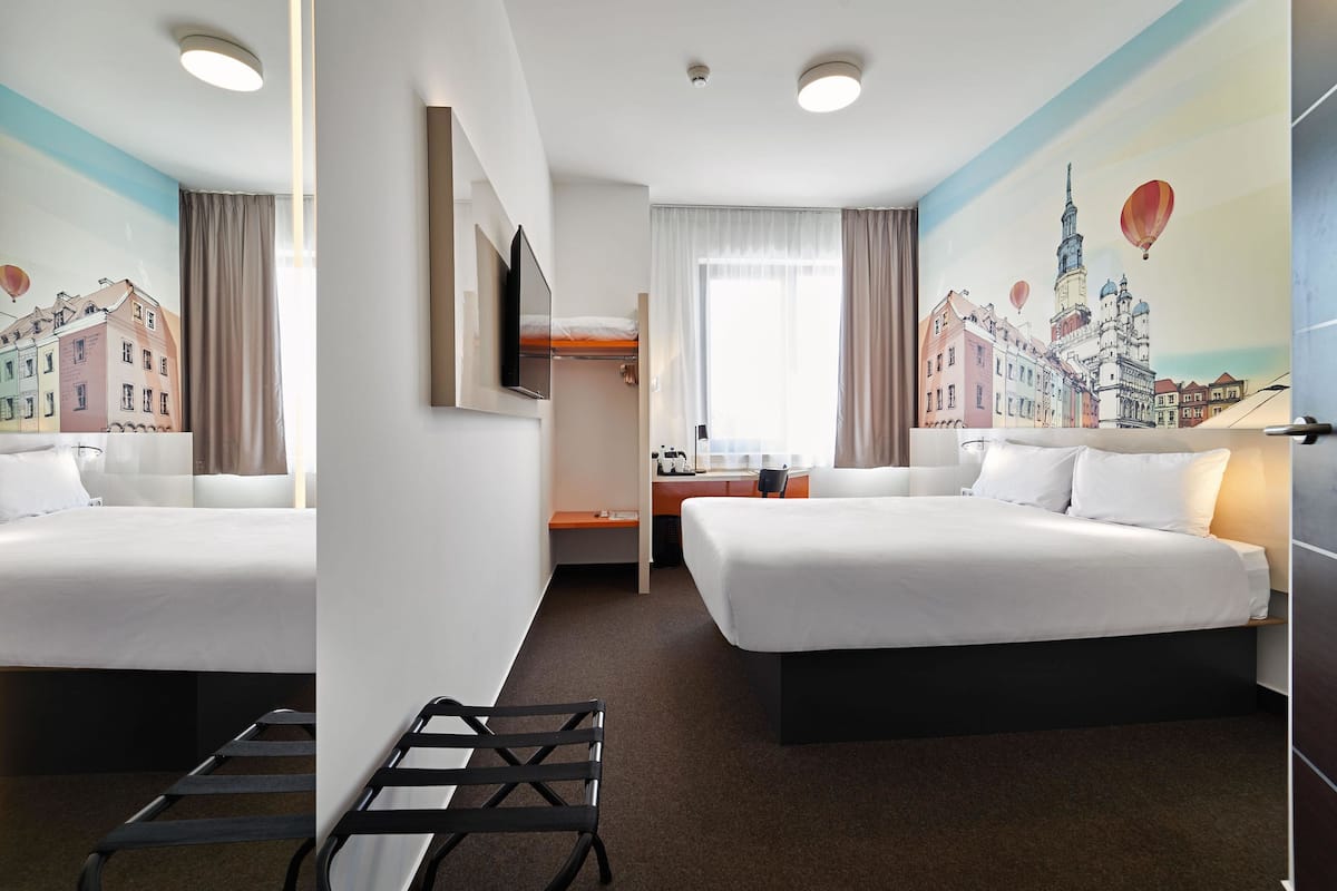 Een hotelkamer met twee bedden, een bureau, een stoel en een groot raam.