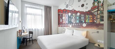A hotel room with a large bed, a desk with a chair, a flat-screen TV, and a mural of a cityscape on the wall.