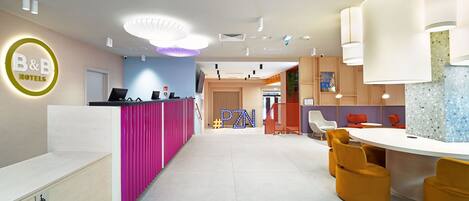 A hotel reception area with a modern design, including a reception desk, a lounge area with seating, and a visible emergency exit sign.