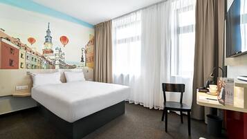 Ein Hotelzimmer mit einem Bett, einem Schreibtisch mit Stuhl, einem Fernseher und einem Wandgemälde einer Stadtansicht.