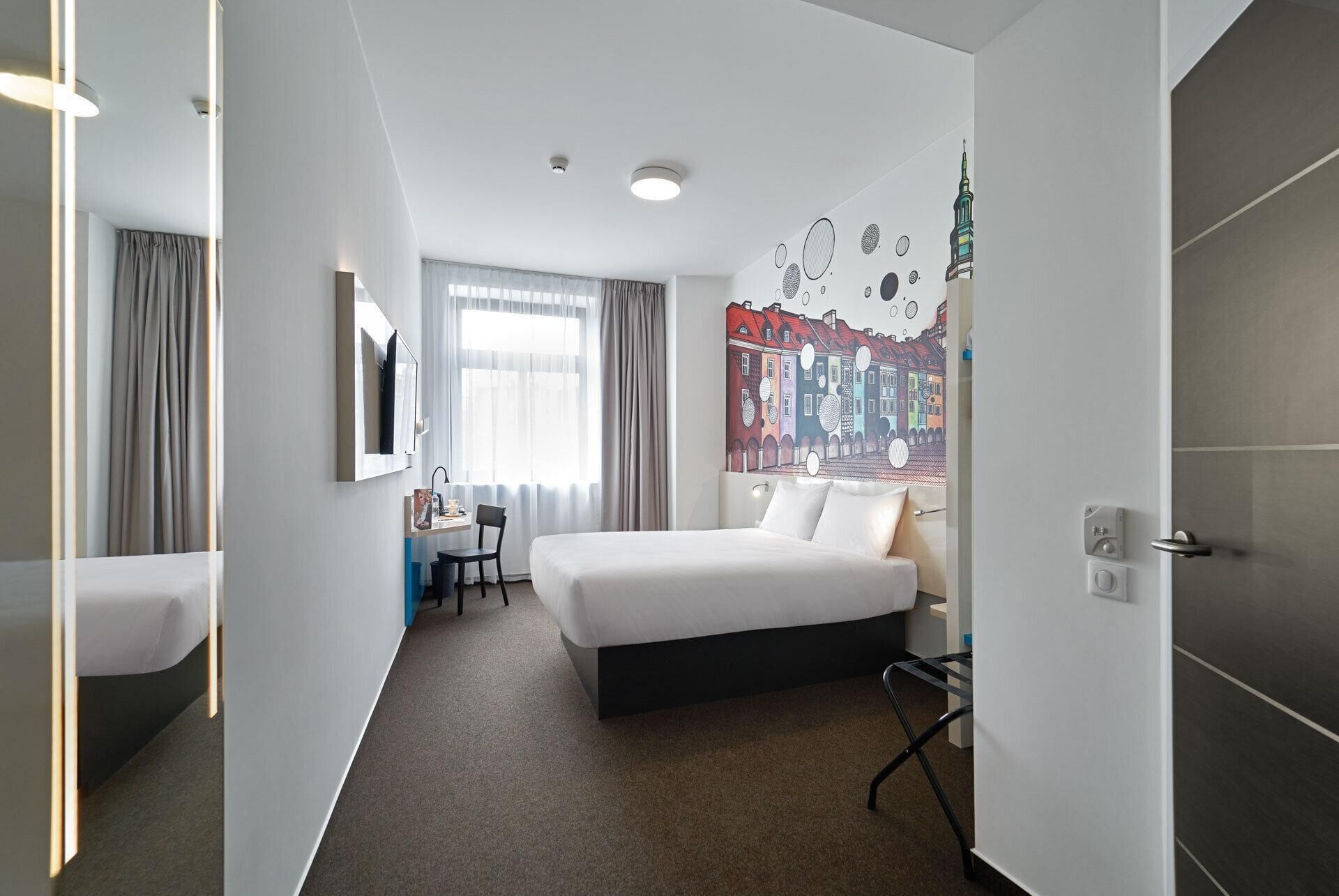 Habitación de hotel con cama, escritorio, silla, televisión y un mural en la pared.