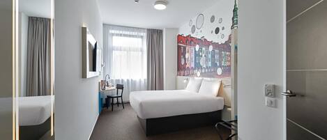 Habitación de hotel con cama, escritorio, silla, televisión y un mural en la pared.