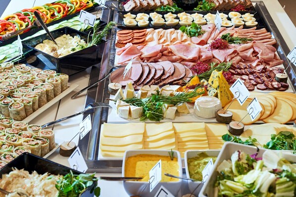 Buffet com diversos alimentos, incluindo carnes, queijos e saladas.