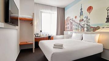 Una habitación de hotel con una cama grande, un escritorio, una silla, un televisor y un mural de un paisaje urbano.